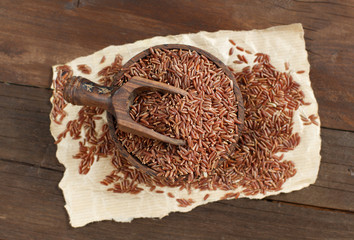 Uncooked Red rice in a bowl with a wooden spoon