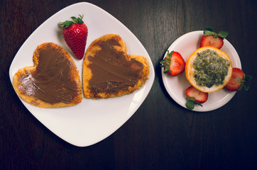 Heartshaped pancakes covered with chocolate and strawberry next to grenadilla sorrounded by cut strawberries, seen from above, elegant breakfast concept