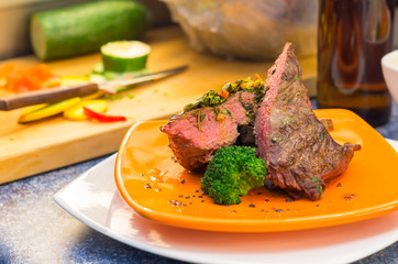 Delicious medium rare sirloin steaks and vegetables placed on orange plate, elegant presentation