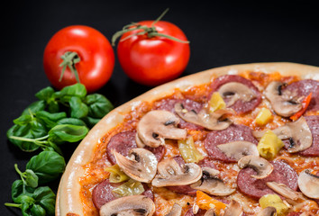 closeup Tasty pizza with tomatoes, cheese, basil and ham on a black background (shallow DOF)
