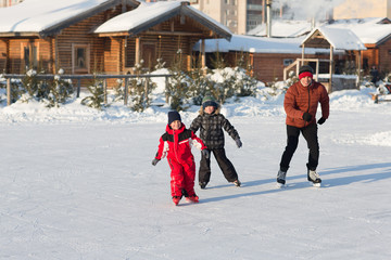 Happy young family skate at the rink in the winter. Beautiful family walking and playing on the ice in winter.