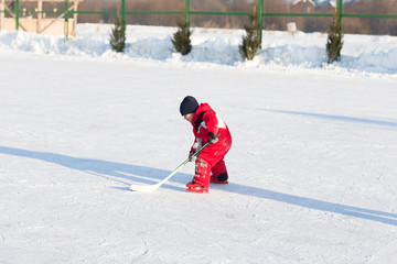 Happy funny kids playing hockey at the rink in the winter. A child with a stick on the ice skating in the winter walks on the street.