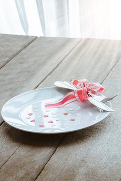 Valentines day table setting with plate, knife, fork, red ribbon