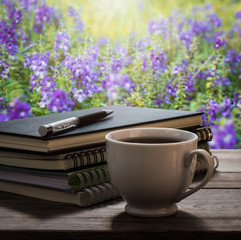 Coffee break with notebooks and pen on wooden table in the garde
