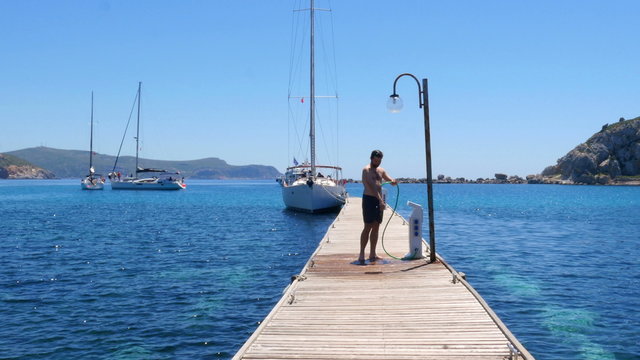 happy man showering on wooden pier at beach after swimming