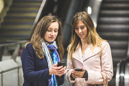 Two women looking at their smartphone on the tube.