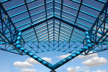 Glass roof with blue metal construction against the blue sky. Lookup.