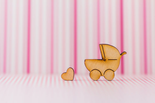 Wooden icon of baby carriage and little heart on pink striped ba