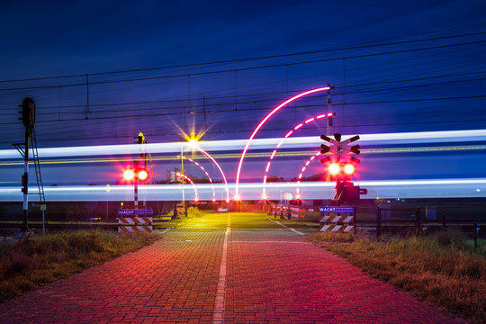 Bewaakte spoorwegovergang met brandende lichten in de nacht en voorbijrijdende trein