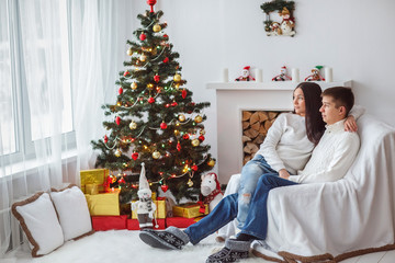 Young beautiful couple playing near a Christmas tree. Loving couple sitting by the fireplace.