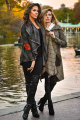 Fototapeta premium Two attractive caucasian women posing against the lake in the autumn park.