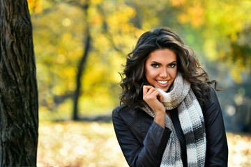 Portrait of smiling woman wearing leather jacket and scarf. Young woman in beautiful autumn park, concept autumn.