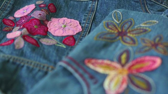 Close up of blue denim jeans girl clothes with beautiful floral decorations and colorful stitches. Structure of denim textile decorated with needlework and fabric applique. Beautiful denim background