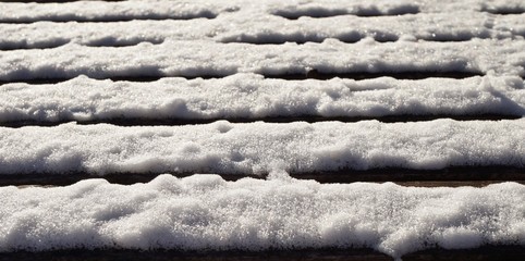 White snow fallen on the horizontal slates of a wooden park bench