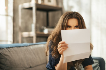 Concentrated young female is sitting on couch reading letter