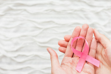 White fabric background with ruche. Woman hands with pink ribbon - symbol of breast cancer awareness. Good as background for World Cancer Day posters, printed materials. Place for text.