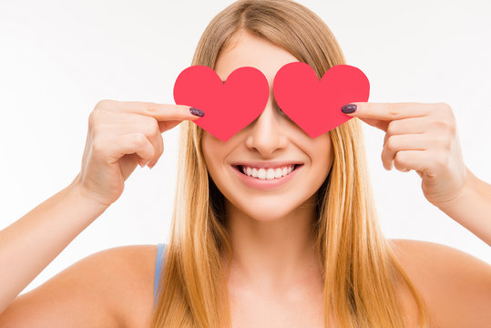 Cheerful young  girl hiding her eyes behind two paper hearts, cl