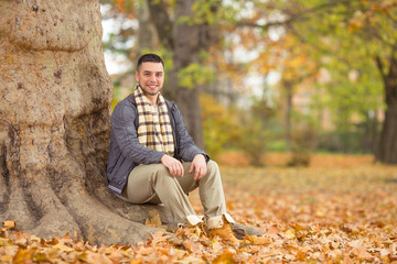 Smiling young man sitting beneath the tree and looking at camera