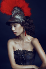 Portrait of beautiful woman in helmet with red feathers n dark studio background
