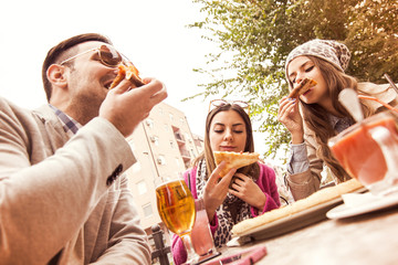 Young group of laughing people eating pizza and having fun
