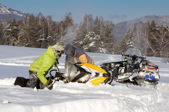 Two athletes pull a snowmobile.
