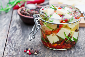 white  cheese cubes and herbs dipped in olive oil in small jar o
