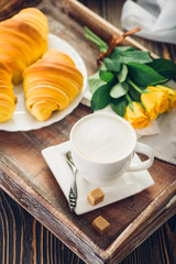 Coffee, croissant and flowers on tray on a wooden table