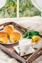 Coffee, croissant and flowers on bed next to the window