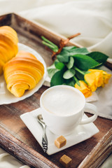 Coffee, croissant and flowers on bed