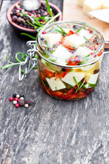 white  cheese cubes and herbs dipped in olive oil in small jar o
