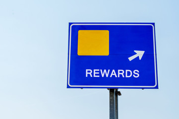 Rewards Blue Road Sign Against Sky
