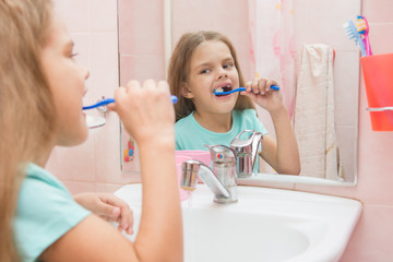 Six year old girl cleans the upper lateral teeth look in the mirror in the bathroom