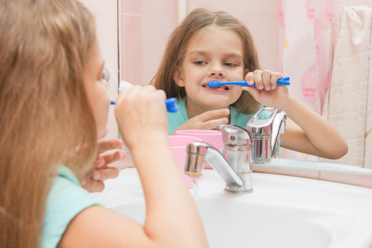 Six year old girl having fun brushing his teeth look in the mirror in the bathroom