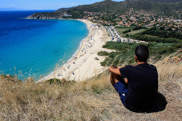A man sitting and watching the panorama os the Solanas Beach and the sea in Sardinia, Italy.
