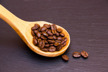 Coffee beans in wooden spoon on slate top