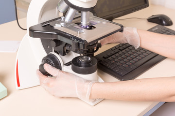 Medical or scientific researcher using a microscope in laboratory environment with test tubes and equipment