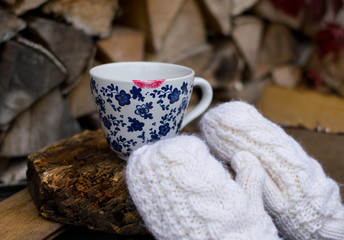 Obraz na płótnie Canvas Cup of tea or coffee with trace of red lipstick in white mittens, gloves, on the wooden table, dishes