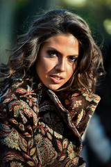 Fashion outdoor portrait of beautiful young woman with dark hair in elegant coat posing in sunny autumn park.