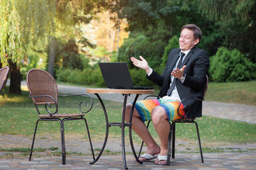 Businessman dressed in suit and shorts working with laptop outdo