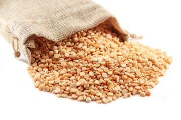 Burlap sack with dried peas spilling out over a white background. 