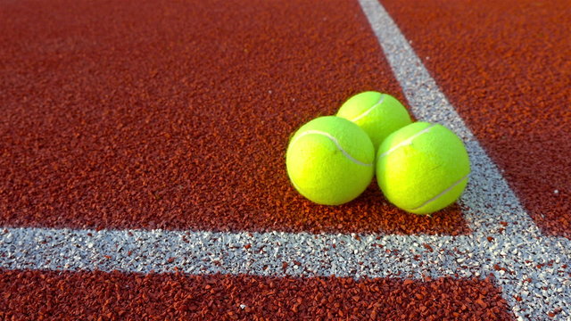 Hand puts three tennis balls on red tennis court