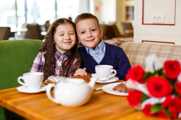 little girl with a baby boy , sitting at the table and drank tea with Cake