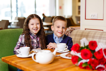 little girl with a baby boy , sitting at the table and drank tea with Cake