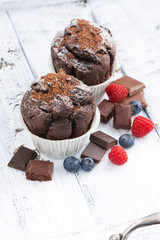 chocolate muffins and fresh berries on white wooden background