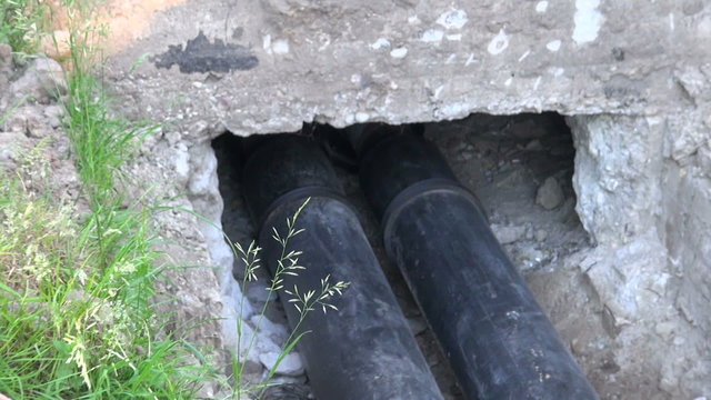 Plastic black central heating plastic pipes in the ditch going into the house