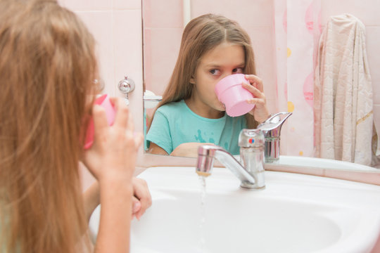 Girl dials the water in the mouth from the cup by rinsing the mouth after brushing