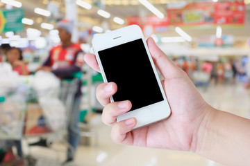 Hand holding mobile phone at supermarket checkout background