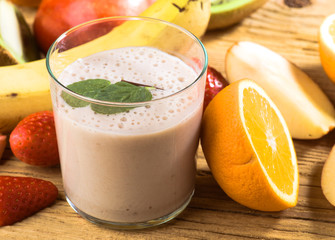 Natural banana smoothie surrounded by fruit on wooden base