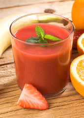 natural strawberry smoothie surrounded by fruit on wooden base