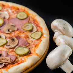 closeup Tasty pizza with mushrooms, ham and pickles on a black b